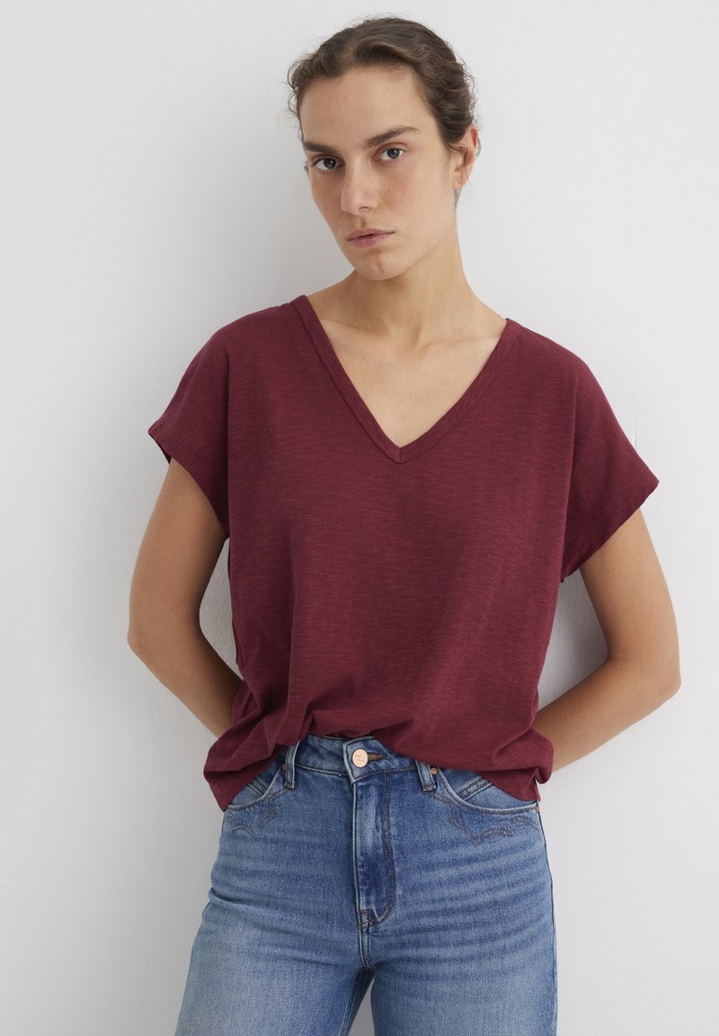 Burgundy V-neck t-shirt with short sleeves, made of lightweight fabric; paired with light blue high-waisted jeans. Smooth, relaxed fit.
