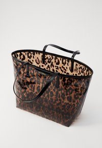 Bolso tote de estampado de leopardo con un exterior negro brillante, interior beige en contraste y dos asas resistentes. Presenta logotipos en el lateral.