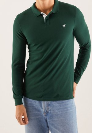 Koszula polo z długim rękawem w ciemnozielonym kolorze, wykonana z bawełny, z białym kołnierzykiem i małym logo ptaka na piersi. Casualowy krój z gładką fakturą.