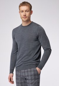 Grauer Langarmpullover aus weichem Strickstoff mit Rundhalsausschnitt und gerippten Bündchen, kombiniert mit karierter Hose.