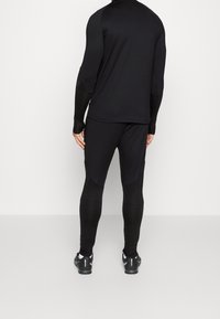 Černý sportovní outfit se dlouhým rukávem a přiléhavými kalhotami s texturovaným vzorem na rukávech a dolních nohou, vyrobený z elastického materiálu.