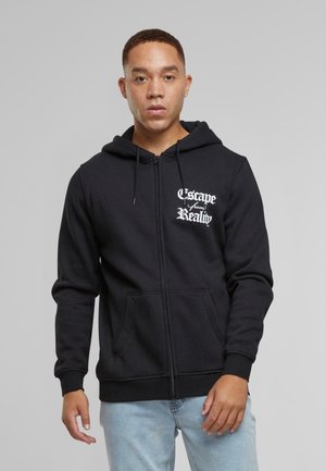Sudadera con cremallera negra, con bolsillos delanteros, capucha con cordones y gráfico de texto blanco "Escapar de la Realidad" en el lado izquierdo del pecho. Textura de tela suave.
