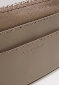 Hnědá kožená peněženka na zip s několika sloty na karty, embosovaným logo a kontrastním stehem. Hladký povrch s minimalistickým designem.