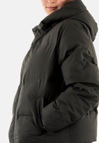 Dunjakke i mat sort med hætte, der har lynlåslukning og sidelommer. Stoffet ser glat og let skinnende ud.