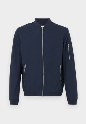 Jachetă bomber de culoare bleumarin, cu fermoar frontal, buzunare cu fermoar pe laterale, buzunar cu fermoar pe mâneca stângă, mansete și guler ribbed.