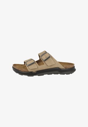 Tan suede slide sandal with adjustable double straps, metal buckles, cork footbed, and black rubber sole.