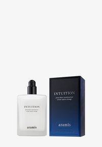 Aftershave-Feuchtigkeitscreme in einer klaren Flasche mit einem schwarzen Pumpverschluss, neben einer blau-schwarzen rechteckigen Box mit weißem Text.