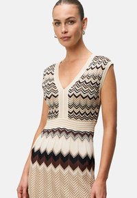 Knit dress featuring a chevron pattern in beige, brown, and black tones with a deep V-neck and cap sleeves, textured fabric with ribbed waist.