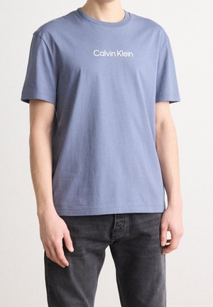 Modrá bavlněná tričko se žíháním, krátkými rukávy a bílým logem "Calvin Klein" na hrudi. Jednoduchý, volný střih a hladká textura.