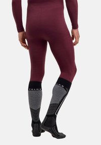 Bordowe długie legginsy w połączeniu z szaro-czarnymi wzorzystymi skarpetkami sięgającymi do kolan. Skarpetki mają kontrastowe logo i teksturowane elementy.