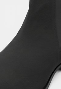 Gros plan d'une bottine en daim noir montrant une texture lisse et des détails de couture sur la partie supérieure.