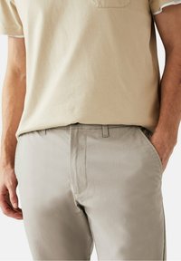 Beige shirt met korte mouwen en een borstzak, gecombineerd met lichtgrijze op maat gemaakte broek met zijzakken en subtiele stikdetails.