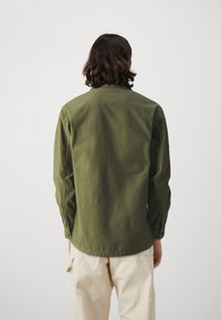 Green cotton shirt with a straight cut, long sleeves, and a round hem. Features buttoned cuffs and a simple collar.