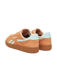 Narancsszínű velúr tornacipők világoskék részletekkel és fehér fűzőkkel. Nagyobb tapadású, texturált gumitalppal rendelkezik, és a sarkán a Reebok logó található.