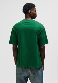 Grön bomull t-shirt med avslappnad passform, rund halsringning och korta ärmar. Buren med lösa, urblekta jeans. Strukturerad tyg synlig.