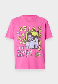 Pink cotton t-shirt featuring a graphic design with black and yellow accents, flowers, peace symbols, and text referencing "De La Soul."
