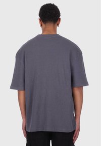 T-shirt gris surdimensionné à manches courtes en tissu côtelé, avec un col sans couture et des épaules tombantes. La vue de dos présente des lignes épurées et un design minimaliste.