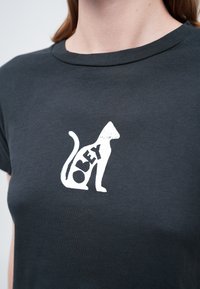 Osoba nosi tamnosivu majicu s bijelom siluetom mačke i riječju "OBEY" integriranom unutar tijela mačke.