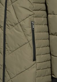 Olivově zelená prošívaná pufovaná bunda s černou zipovou kapsou, která se vyznačuje geometrickým prošíváním a hladkým povrchem.