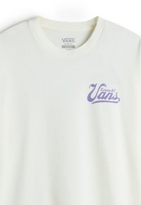 Camiseta blanca de corte holgado con un logo morado de Vans en el lado izquierdo del pecho. Tejido suave con cuello redondo y mangas cortas.