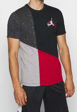 Homme portant un T-shirt à manches courtes avec des blocs de couleur noir, blanc et rouge présentant un motif d’éclaboussures de peinture et un petit motif graphique Nike Air sur la poitrine.