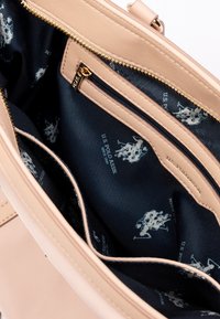 Světle růžová kabelka s hladkým koženým exteriérem, se tmavě modrou textilní podšívkou zdobenou opakujícími se bílými logy a zipovými kapsami.