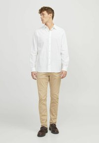 Hvid langærmet skjorte med knapper lavet af let stof, parret med beige slim-fit bukser og mørkebrune sko. Enkel design og neutrale farver.