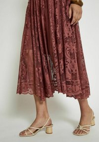 Gonna midi in pizzo rosa polveroso, con motivi intricati e orlo scallop, abbinata a sandali a tacco basso beige chiaro.