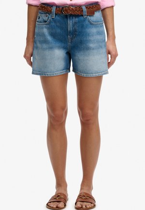 Personne portant un short en jean bleu délavé avec une ceinture tressée marron, une chemise rose rentrée et des sandales en cuir marron.