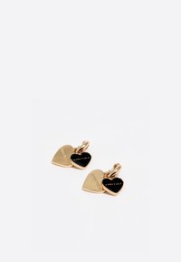 Pendientes de oro en forma de corazón con un corazón negro mate que lleva grabado el texto "Simbary Lola" y "Chanelcia". El diseño incluye un sencillo enganche en forma de aro.