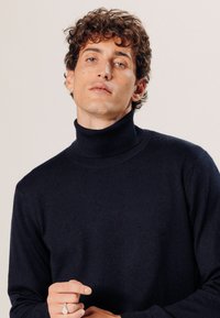 Marineblauer Rollkragenpullover aus weichem Material, mit einem taillierten Schnitt und gestrickter Textur. Runde Kragen und gerippte Bündchen.