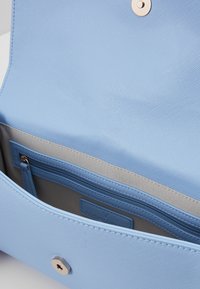 Ljusblå strukturerad handväska med klaffstängning, som har en innerficka, en ficka med dragkedja och grå foder. Gyllene detaljer synliga.