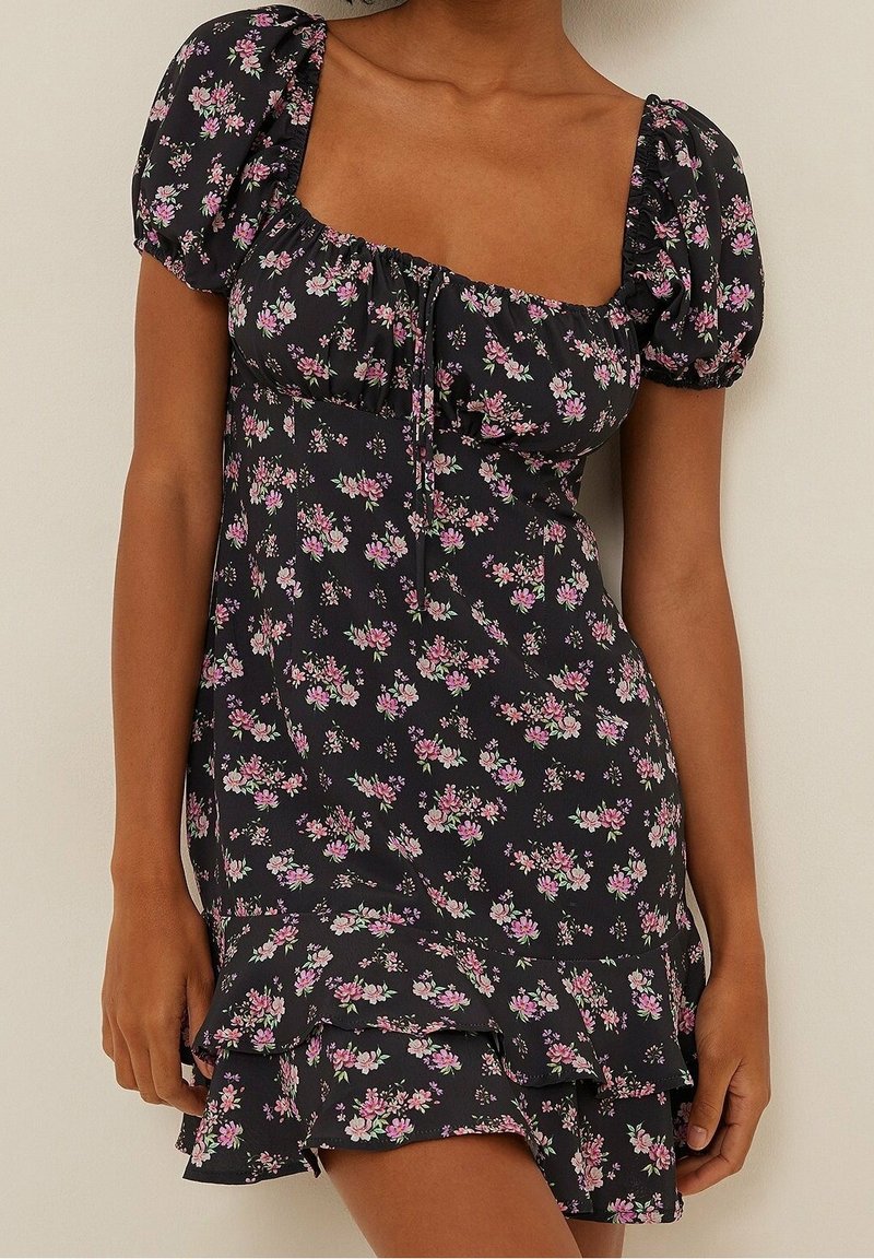 Černé květinové šaty s balónovými rukávy, hranatým výstřihem a volánkovým střihem ve vrstvách. Na látce jsou malé růžové a bílé květinové vzory.
