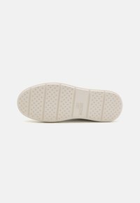 Semelle de chaussure avec une surface texturée, couleur beige clair, présentant des rainures latérales et de petits motifs en forme de cœur. Marque gravée sur le côté.