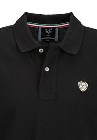 Zwarte polo met een geribbelde kraag, een sluiting met twee knopen en een geborduurd schildlogo. Is voorzien van een gestreepte binnenkraag in groen, wit en rood.