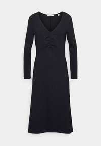Robe noire à manches longues avec un col en V, présentant un détail froncé à la taille et un tissu lisse et texturé. Longueur midi.