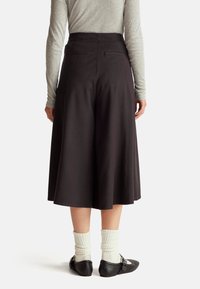 Czarne szorty o wysokim stanie z ukrytymi tylnymi kieszeniami, w połączeniu z prążkowanymi białymi skarpetkami i czarnymi balerinami, widok od tyłu.