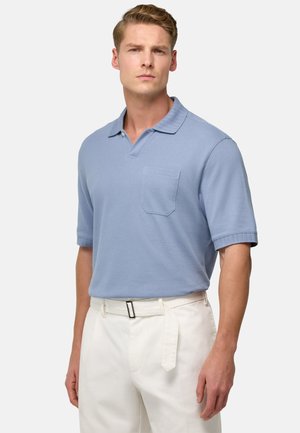 Polo shirt azzurro chiaro a maniche corte con colletto a costine e tasca. Indossato con pantaloni bianchi dotati di cintura. Tessuto morbido, design casual.