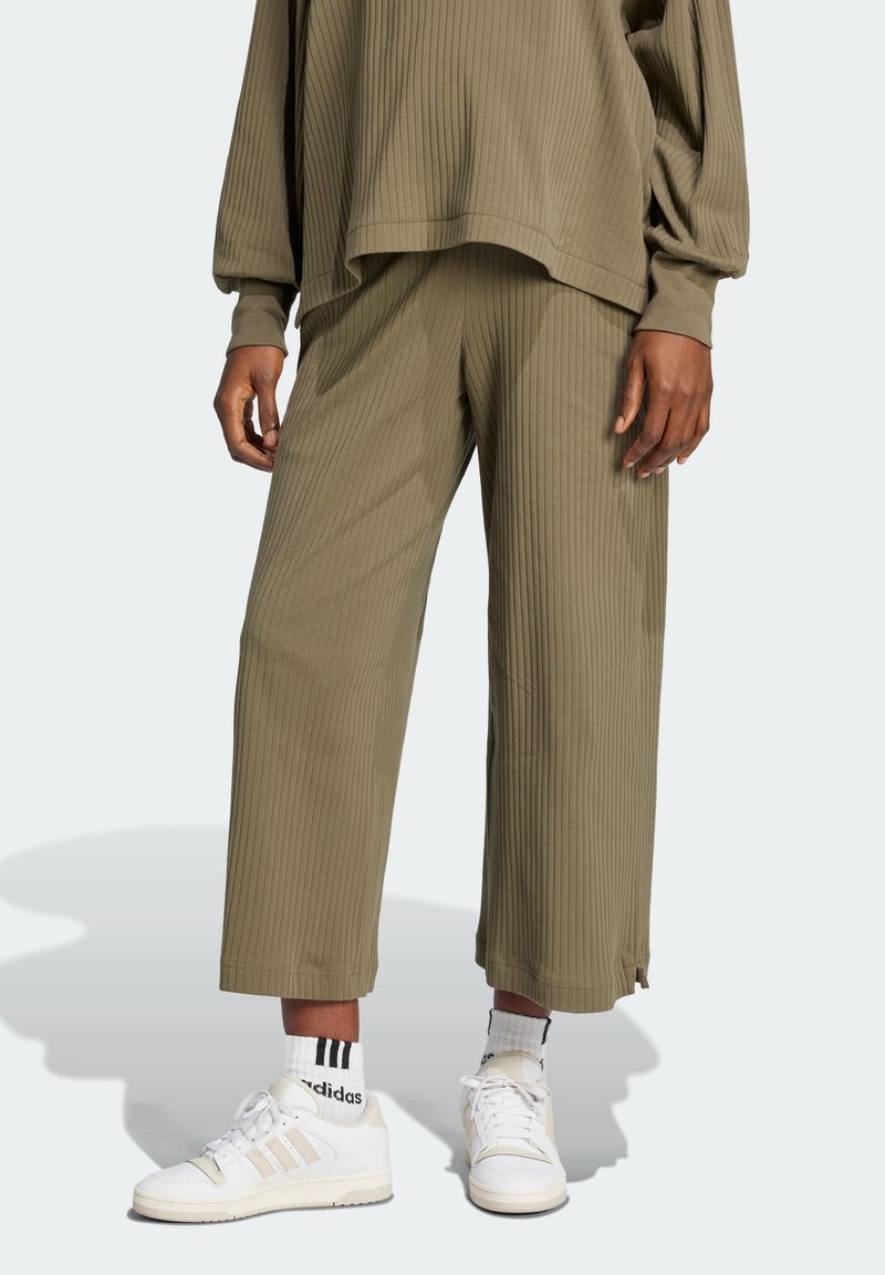 Olivgrön ribbad stickad topp och matchande lösa byxor, med en texturerad yta och sidofickor, tillsammans med vita sneakers.