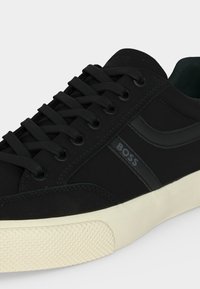 Baskets basses noires avec lacets noirs, semelle en caoutchouc crème et logo "BOSS" sur le côté.