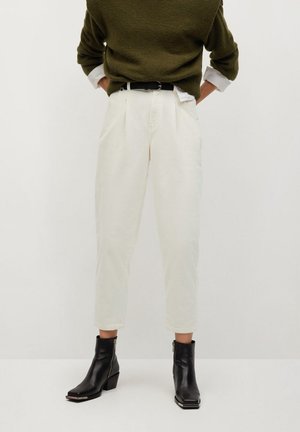 Persoon die witte corduroy broek met hoge taille draagt, een zwarte riem, een donkergroene trui en zwarte enkellaarsjes met ritsen.