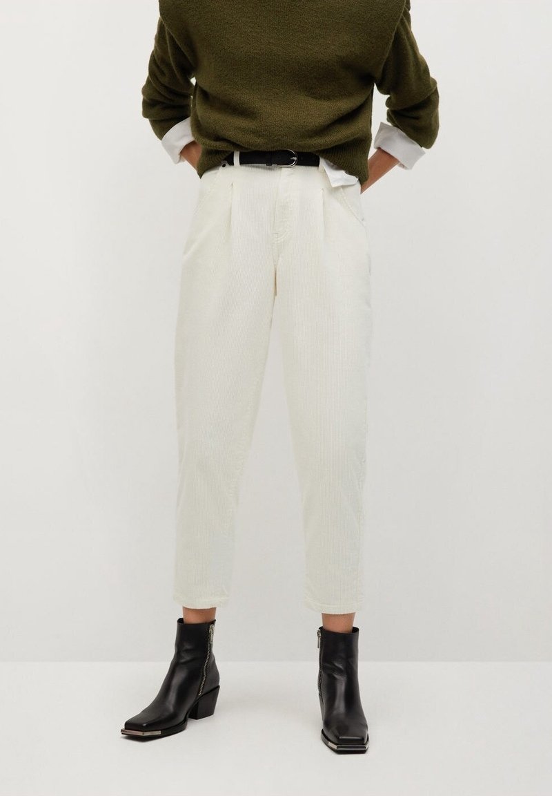 Personne portant un pantalon en velours côtelé blanc taille haute avec une ceinture noire, un pull vert foncé et des bottines noires à fermeture éclair.