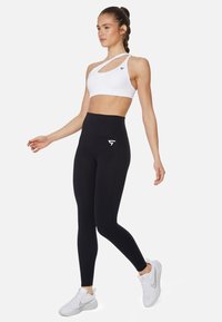 Leggings neri a vita alta con design elegante e tasca laterale, abbinati a un reggiseno sportivo bianco asimmetrico con logo.
