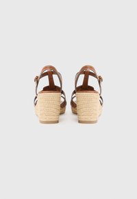 Brown leather wedge sandals with braided jute heel, adjustable ankle strap, and open heel design. Textured surface and smooth finish.