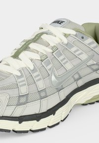Γκρι και λευκό αθλητικό παπούτσι Nike με πλέγμα, παχιά σόλα, λευκά κορδόνια και ασημένιο λογότυπο Nike swoosh στο πλάι.