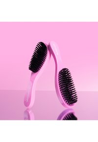 Różowe szczotki do włosów z czarnymi szczecinkami i eleganckim, zakrzywionym kształtem, odbijające się na lustrzanej powierzchni na różowym tle.