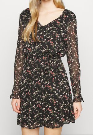 Sort blomsterkjole med lange gennemsigtige ærmer, V-udskæring, talje med bindebånd og mønster af små lyserøde og hvide blomster.