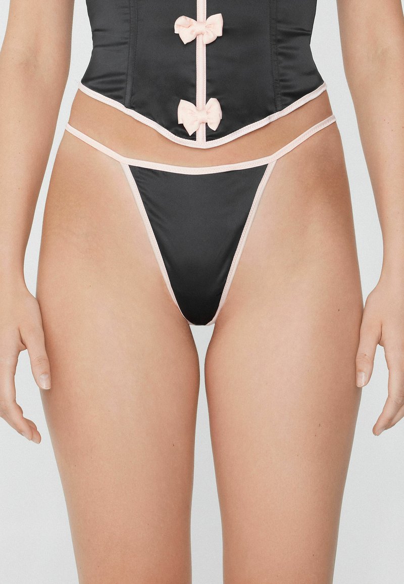 Schwarzer Satin-Tanga mit rosa elastischen Besätzen und Schleifen. Verfügt über ein tief sitzendes Design und minimalen Schutz. Die glatte Textur erhöht den Komfort.