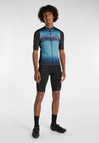 Herre cykeloutfit med en blå gradienttrøje med geometriske mønstre, korte ærmer, lynlås foran og sorte polstrede shorts.