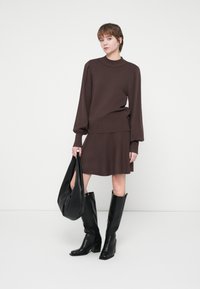Brun strikket sweater med puffærmer, parret med en matchende brun nederdel. Båret med knæhøje sorte læderstøvler og en sort tote taske.